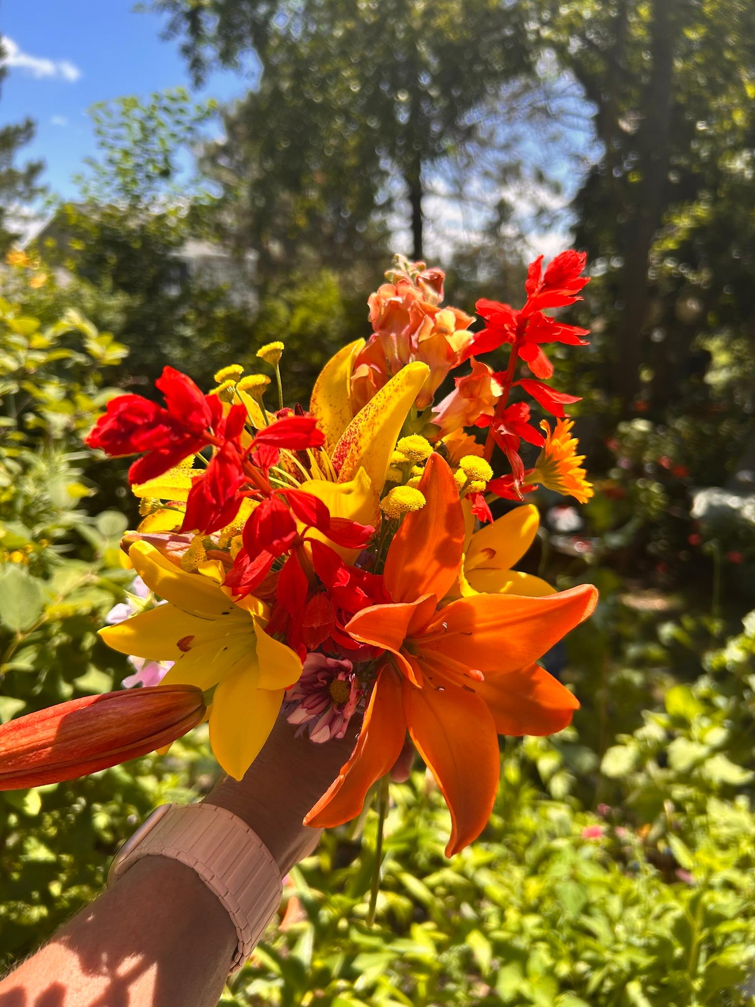 Bright orange and yellow lily bouquet held in a sunny garden.