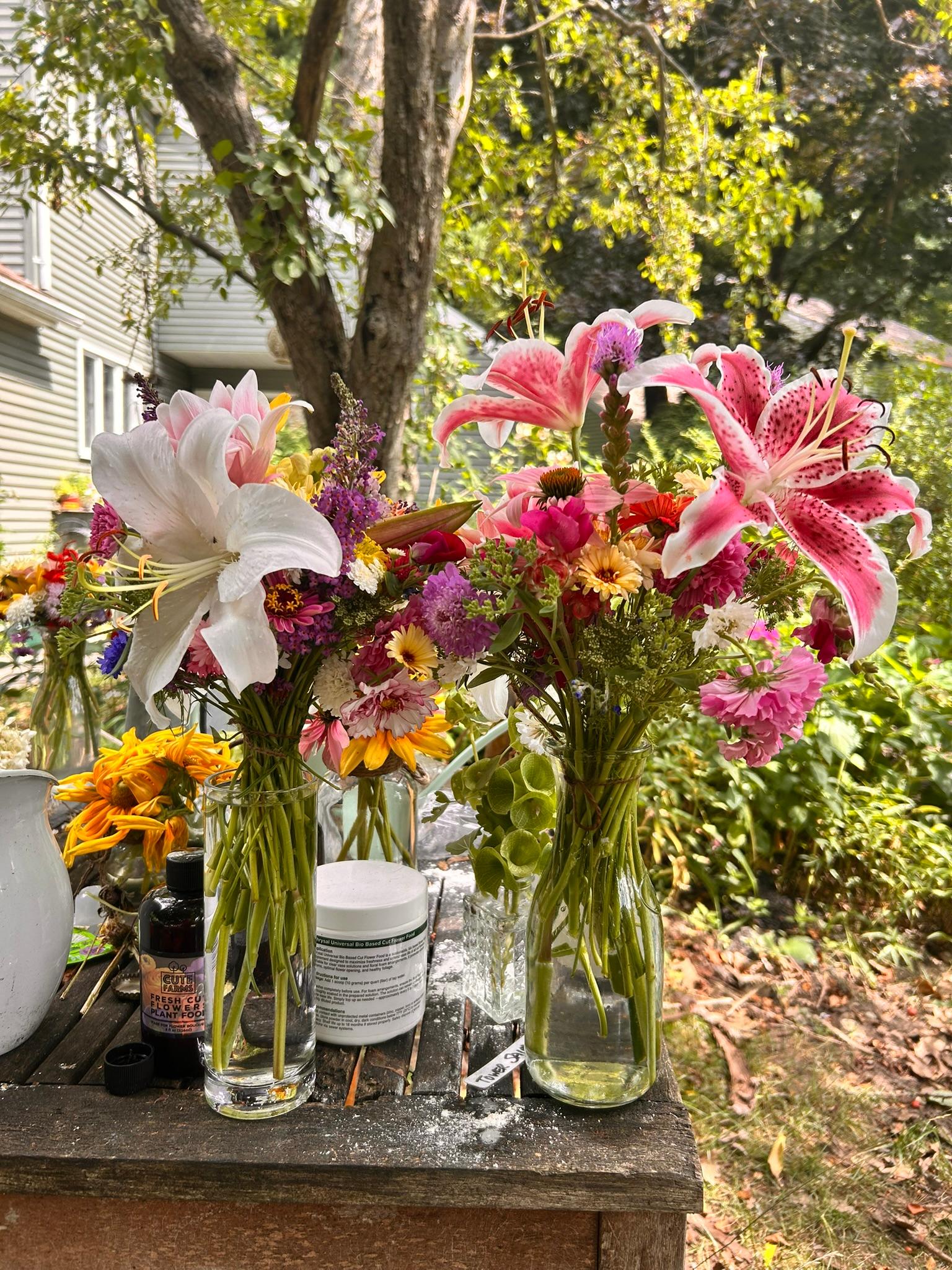 Two bright summer bouquets with white and pink lilies arranged on a garden table.