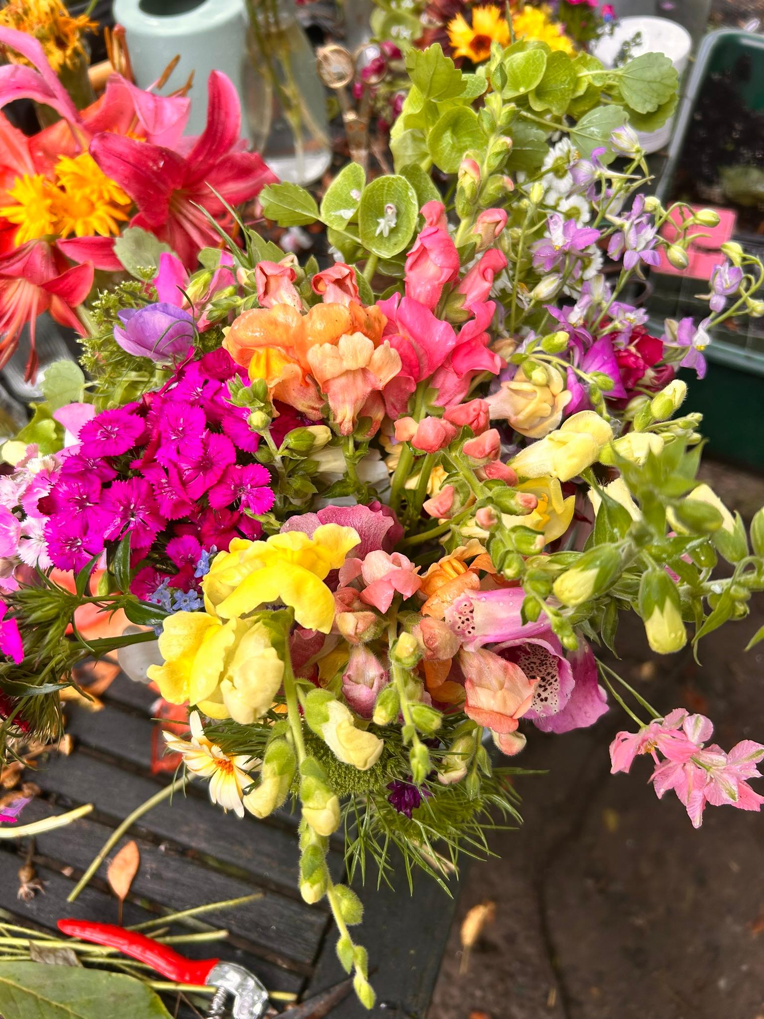 Colorful bouquet with snapdragons, dianthus, lilies, and purple accents on a garden table.
